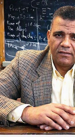 Portrait of Ahmed Gomaa, physics educator, in front of a physics blackboard